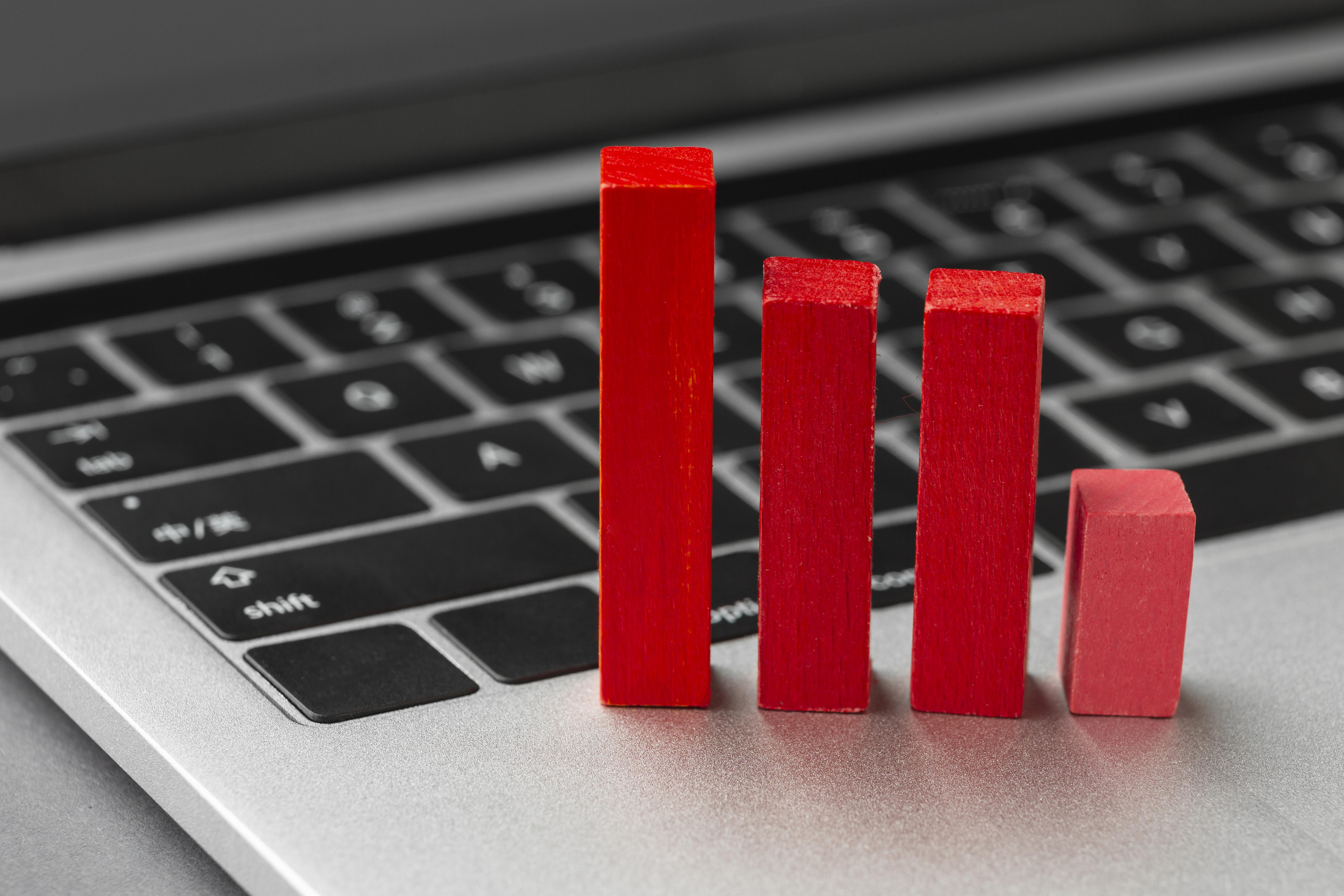 A close-up of a laptop keyboard with four red wooden blocks of varying heights placed on it, representing a bar chart or declining statistics. The background is blurred, and the image conveys a concept related to business, analytics, or digital marketing trends. A close-up of a laptop keyboard with four red wooden blocks of varying heights placed on it, representing a bar chart or declining statistics. The background is blurred, and the image conveys a concept related to business, analytics, or digital marketing trends.